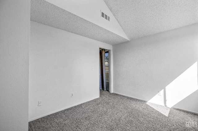 empty room featuring visible vents, baseboards, carpet, vaulted ceiling, and a textured ceiling