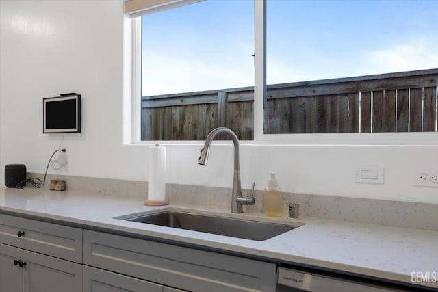 kitchen with dishwasher, sink, light stone counters, and gray cabinets