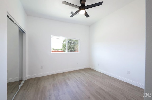 unfurnished bedroom featuring wood finished floors, a closet, ceiling fan, baseboards, and visible vents