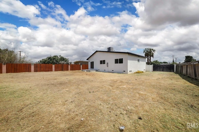 back of property with a fenced backyard, stucco siding, cooling unit, and a lawn