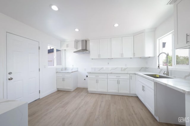 kitchen with wall chimney exhaust hood, a sink, white cabinets, and plenty of natural light