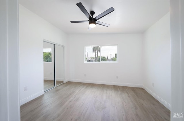 unfurnished bedroom with wood finished floors, a closet, a ceiling fan, and baseboards