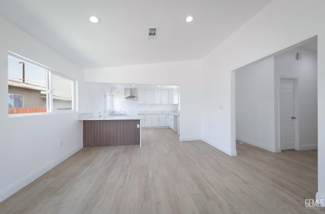 kitchen with a peninsula, light wood-type flooring, baseboards, visible vents, and wall chimney exhaust hood