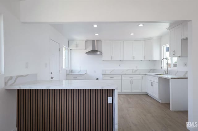 kitchen featuring light stone counters, a peninsula, wall chimney exhaust hood, and a sink