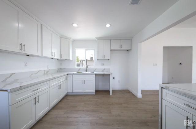 kitchen with light stone countertops, visible vents, white cabinets, and light wood-style floors