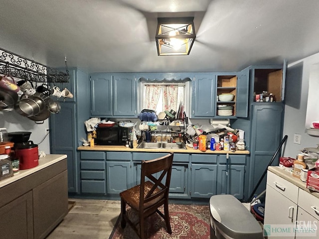 kitchen with a sink, wood finished floors, black microwave, and light countertops