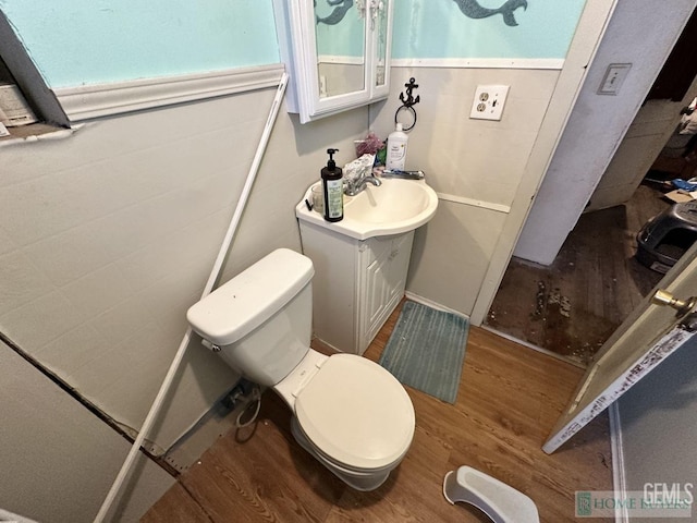 half bathroom with toilet, wood finished floors, and vanity