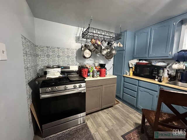 kitchen with blue cabinetry, black microwave, stainless steel gas stove, light countertops, and light wood-style flooring