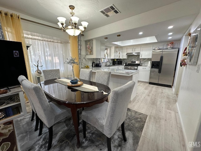 dining room with visible vents, a raised ceiling, light wood-style flooring, a notable chandelier, and recessed lighting