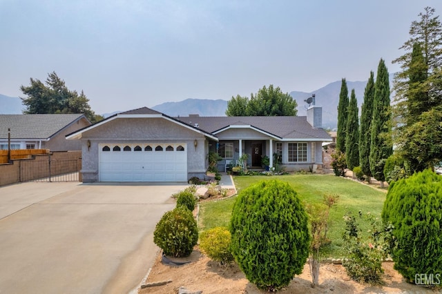 single story home featuring an attached garage, fence, a mountain view, driveway, and a front lawn