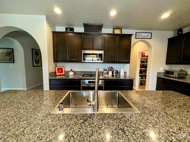 15209 Aldridge Ave, Bakersfield, CA 93314 - kitchen featuring stainless steel appliances, arched walkways, dark brown cabinetry, recessed lighting, and dark stone countertops