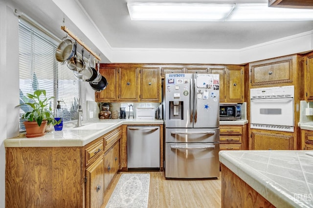 kitchen with ornamental molding, stainless steel appliances, sink, tile countertops, and light hardwood / wood-style flooring