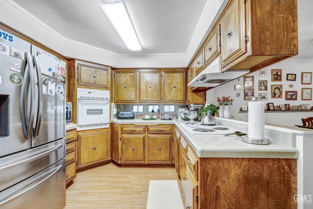 kitchen featuring white appliances, exhaust hood, crown molding, light wood-type flooring, and kitchen peninsula