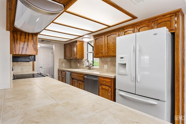 kitchen featuring a sink, stainless steel dishwasher, white refrigerator with ice dispenser, and decorative backsplash