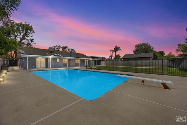 pool at dusk with fence, a diving board, a patio area, and a fenced in pool