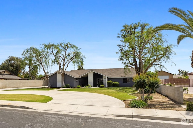 mid-century home with fence, a front lawn, and curved driveway