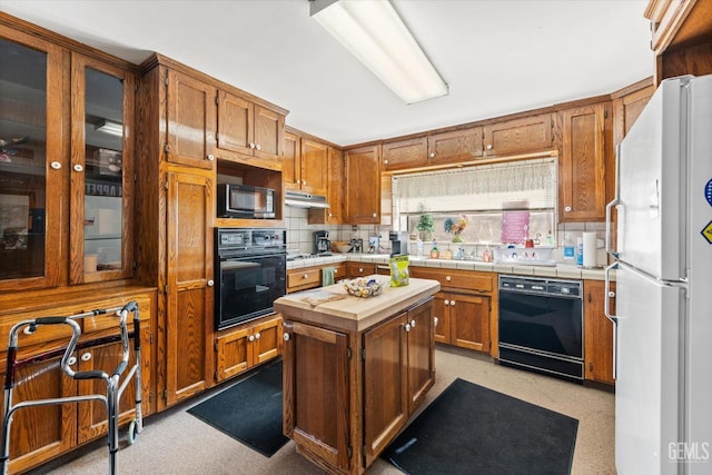 kitchen featuring tile countertops, decorative backsplash, a center island, and black appliances