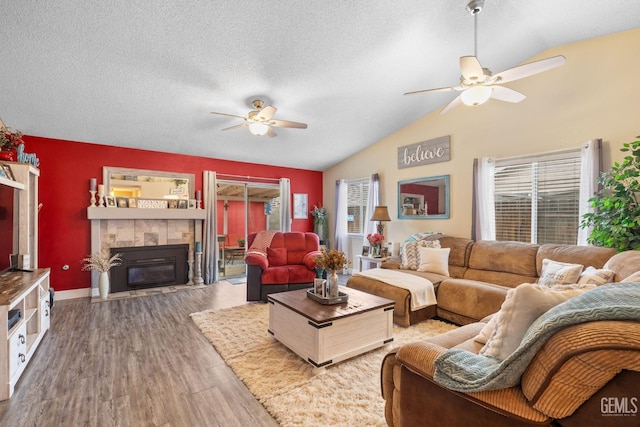 living area with a textured ceiling, a ceiling fan, wood finished floors, lofted ceiling, and a tile fireplace