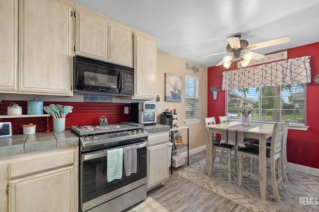 kitchen with light brown cabinetry, stainless steel electric range, black microwave, ceiling fan, and baseboards