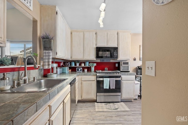 kitchen featuring light wood-style floors, a sink, a textured wall, and stainless steel appliances