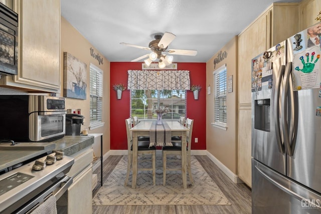 kitchen featuring wood finished floors, light brown cabinetry, baseboards, a ceiling fan, and appliances with stainless steel finishes