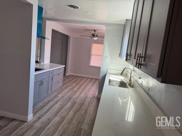 kitchen featuring light stone countertops, sink, ceiling fan, wall chimney range hood, and light hardwood / wood-style flooring