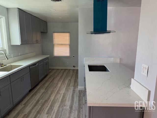 kitchen featuring gray cabinetry, dishwasher, sink, light hardwood / wood-style flooring, and wall chimney exhaust hood