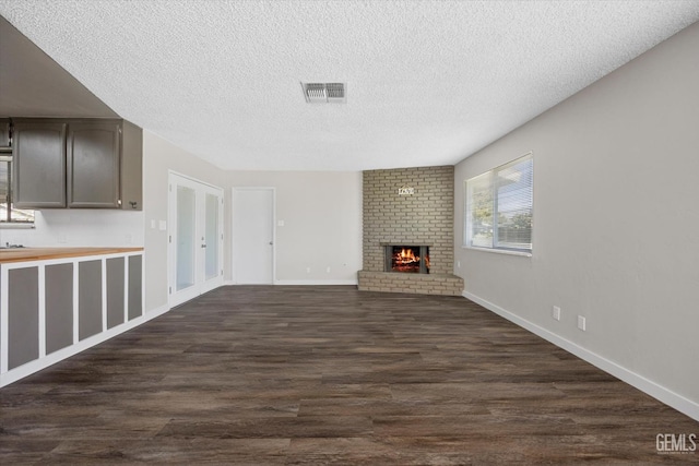 unfurnished living room featuring a brick fireplace, dark hardwood / wood-style floors, and a textured ceiling