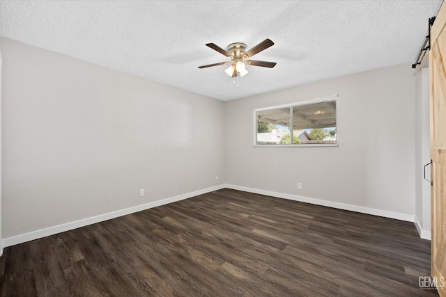 unfurnished room featuring ceiling fan, a barn door, dark hardwood / wood-style floors, and a textured ceiling