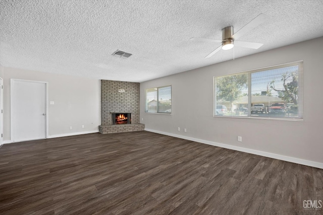 unfurnished living room featuring a brick fireplace, a textured ceiling, dark wood-type flooring, and ceiling fan