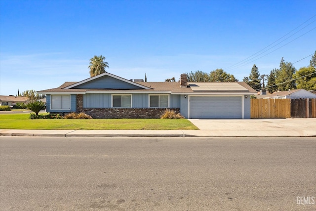 single story home with a garage, a front yard, and solar panels