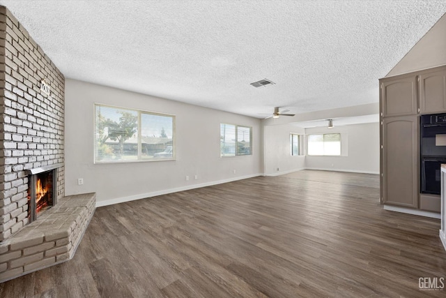 unfurnished living room with dark hardwood / wood-style floors, ceiling fan, a fireplace, and a textured ceiling