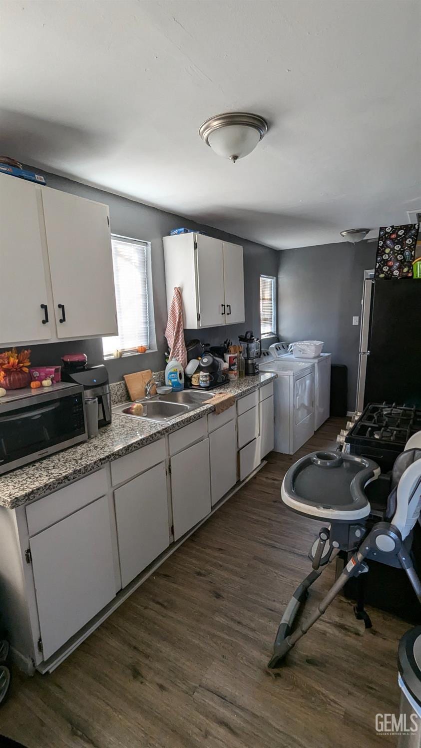 kitchen featuring sink, dark hardwood / wood-style floors, washer and clothes dryer, white cabinets, and appliances with stainless steel finishes