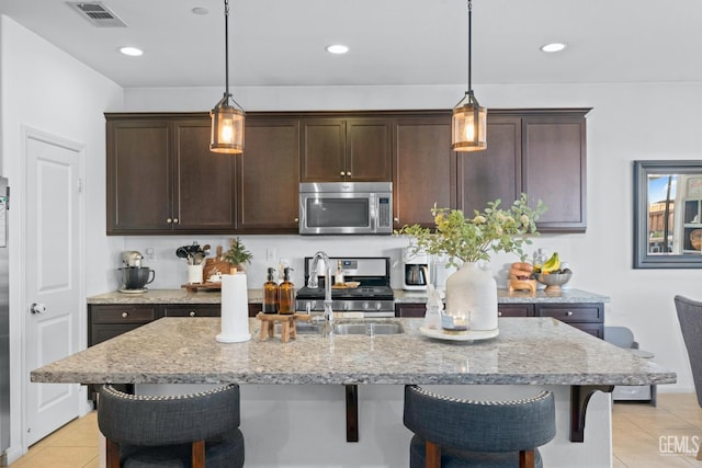 kitchen featuring light stone counters, visible vents, a breakfast bar, appliances with stainless steel finishes, and decorative light fixtures