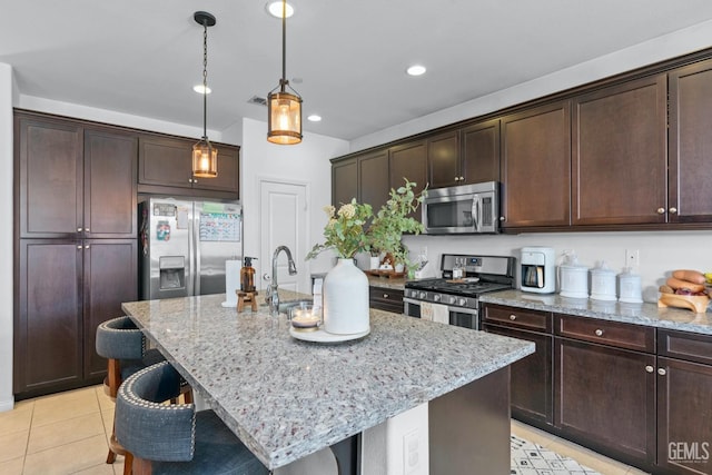 kitchen featuring dark brown cabinets, light stone countertops, a breakfast bar, light tile patterned floors, and appliances with stainless steel finishes