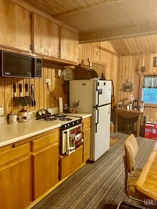 kitchen with wood walls, white appliances, wooden ceiling, dark colored carpet, and vaulted ceiling with beams