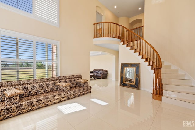 tiled living room with arched walkways, a towering ceiling, stairs, and recessed lighting