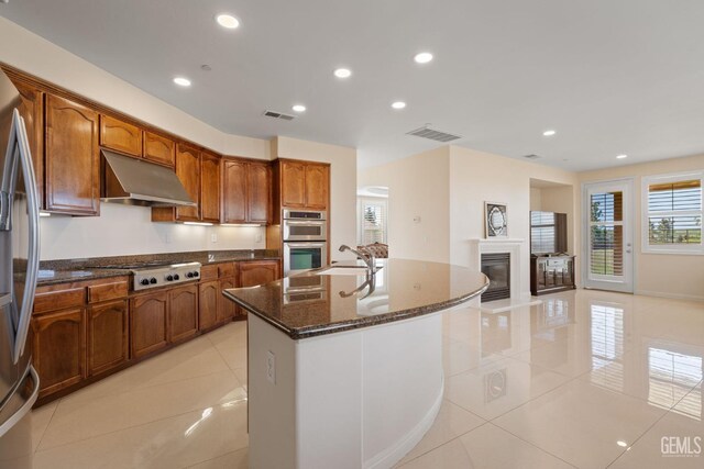 kitchen with dark stone counters, light tile patterned floors, stainless steel appliances, under cabinet range hood, and visible vents