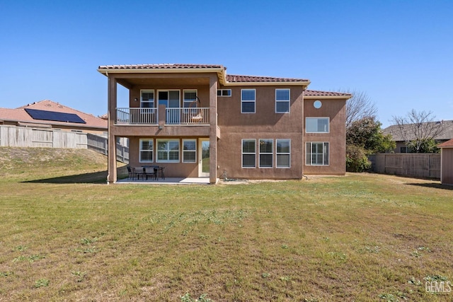 rear view of property featuring stucco siding, a yard, a balcony, and a fenced backyard