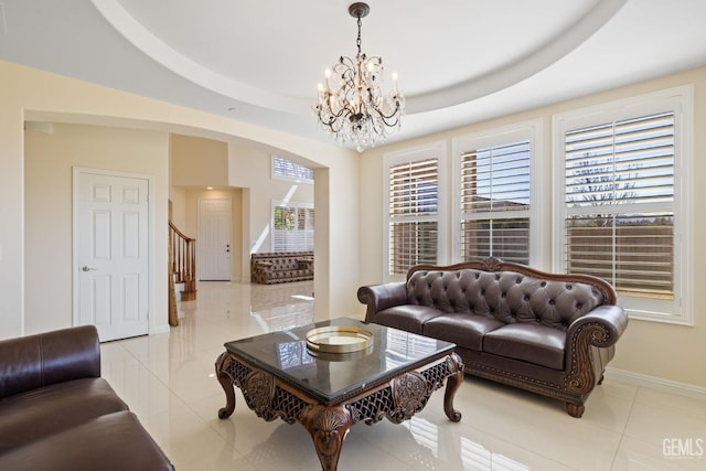 living area with stairway, a tray ceiling, light tile patterned flooring, baseboards, and a chandelier