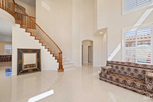 interior space featuring tile patterned floors, baseboards, a high ceiling, and arched walkways