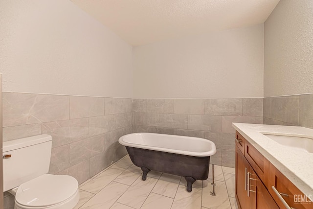 bathroom featuring vanity, a tub to relax in, toilet, and tile walls