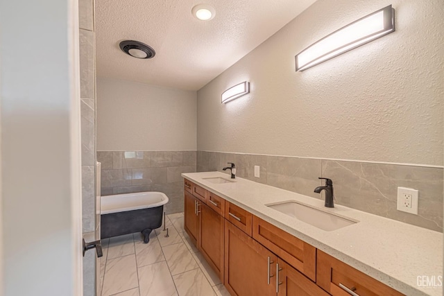 bathroom with vanity, a bathtub, a textured ceiling, and tile walls