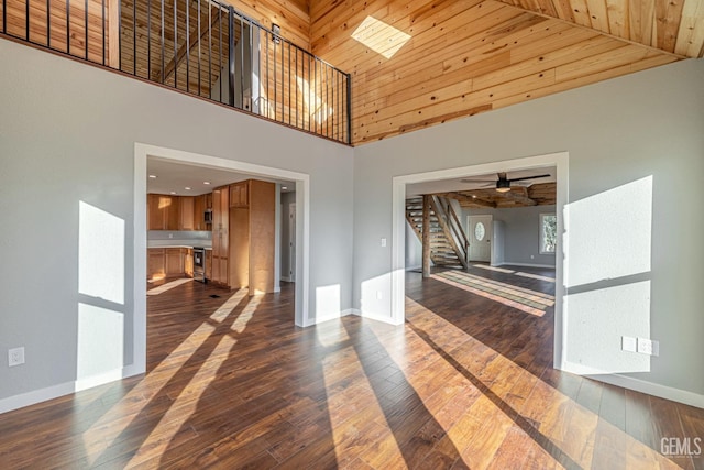 interior space with dark hardwood / wood-style floors, ceiling fan, wood ceiling, and a high ceiling