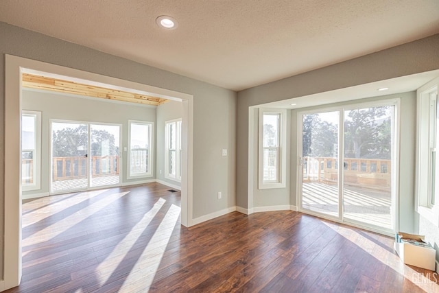 unfurnished room featuring a textured ceiling, a healthy amount of sunlight, and dark hardwood / wood-style floors