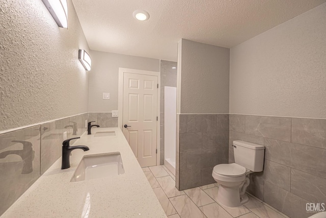 bathroom featuring a textured ceiling, vanity, toilet, and tile walls