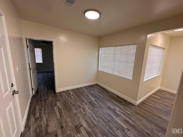 unfurnished room with dark wood-style flooring, visible vents, and baseboards