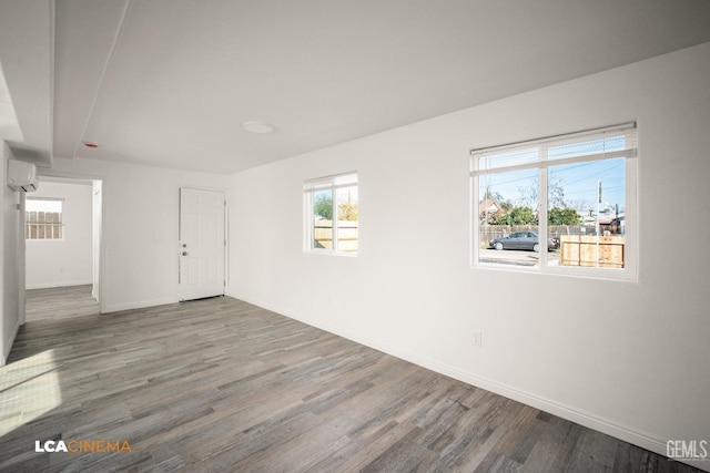 spare room featuring a wall unit AC, baseboards, and wood finished floors