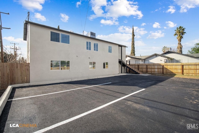 exterior space featuring stairway, uncovered parking, fence, and stucco siding