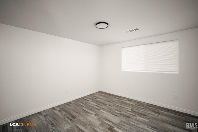 unfurnished room with dark wood-style flooring, visible vents, and baseboards